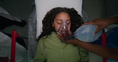 The patient is lying on a gurney with her eyes closed. The nurse gives her air through an oxygen mask. View from above. Emergency resuscitation photo