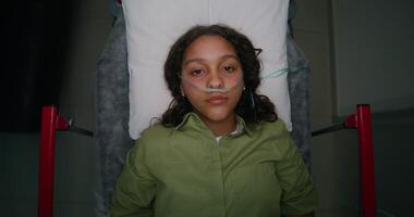 A woman with a breathing tube in her nose is lying on a gurney, top view. She is being driven down the hospital photo