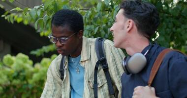 Two young men with backpacks on their shoulders are talking while sitting outdoors. photo