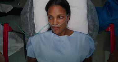 A woman with a breathing tube in her nose is lying on a gurney, top view. photo