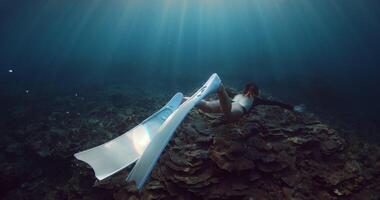 Woman with fins swims underwater on coral reef with sun light in Raja Ampat video