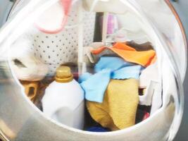 Laundry machine with clothes and cleaning product. Represents chores, routine, domesticity, and cleanliness. Use for articles on home life, cleaning, and lifestyle topics. photo