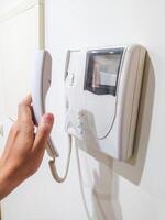 Hand holding an intercom handset on a white wall. Symbolizes security, communication, access control. Use for articles about home safety or apartment living. photo