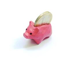 Conceptual image symbolizing savings and finance. A pink handmade piggy bank receives a coin,isolated against white. Represents childhood savings,investment and thrift. photo