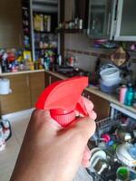 Hand holding a spray bottle in a cluttered kitchen. Symbolizes cleaning, chores, and household tasks. Useful for illustrating hygiene, sanitation, and domestic life. photo