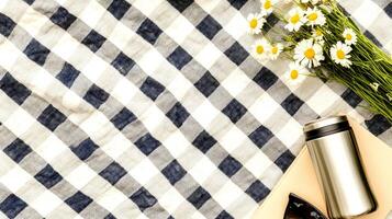 Enjoying a peaceful picnic on a checkered blanket adorned with a thermos and a bouquet of fresh daisies under the sun. photo