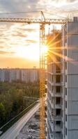 Cranes tower over a construction site as the sun sets, casting warm light on the developing structure and surrounding landscape photo