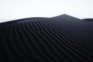 Experience the striking beauty of black sand dunes at twilight featuring smooth, flowing lines accentuated by the soft light above photo
