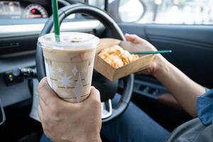 lady holding ice coffee and bread bakery in car dangerous and risk an accident. photo