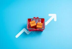A shopping cart with boxed goods and an arrow pointing up. Increased consumption. High prices, rising inflation. Purchasing behavior trends. Cost of living, and market analysis. photo