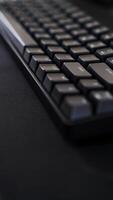 A close-up of a sleek black keyboard with square keys, resting on a dark, textured surface. The keyboard's sharp angles and minimalist design photo