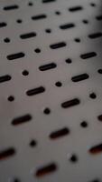 A close-up of a perforated metal surface with a repeating pattern of oval and circular holes. The dark, industrial aesthetic creates a sense of mystery and intrigue. The image photo