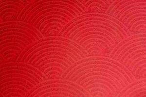 Red textured surface with repeating semi-circular wave patterns, resembling traditional Japanese motifs. photo