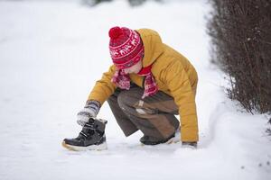 A little boy sits in the snow and puts on a boot. Child in winter. photo