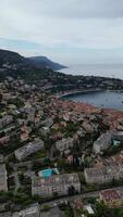 Aerial view of a coastal town with terracotta rooftops, surrounded by hills and the sea. The sky is overcast, creating a serene atmosphere. video