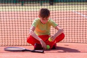 The child sits at the net with a racket photo