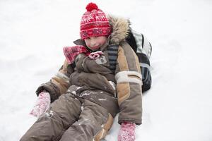 Funny boy in winter goes to school with a backpack.A little boy with a schoolbag sits in a snowdrift. photo