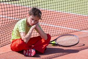 The boy lost the tennis competition The child sits at the net with a racket. Psychology of sports in childhood. photo