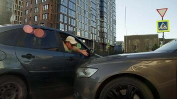 Bearded man, leaning out of window of his car, is arguing with careless driver who has just crashed into his car while driving in city. video