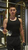 Well-trained Asian athlete performs bicep exercises with dumbbells during a workout at gym. veins in his arms are visible and protruding due to tension. video
