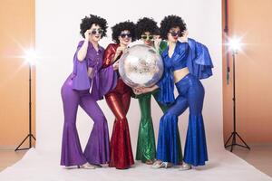 Three female pop stars in neon clothes pose in front of a silver ball in a studio. Group of girls in the style of the seventies. photo