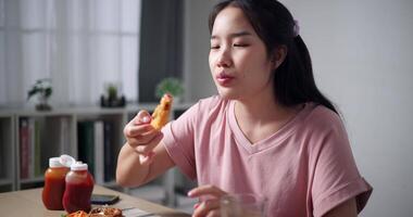 Handheld shot, Asian woman enjoying lunch of fried food and soda on wooden table in living room at home. Lifestyle concept. Enjoying fried food. video