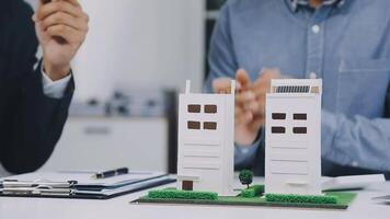 Two people are sitting at a table with a model of a building video