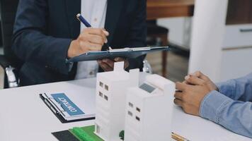 A real estate agent is writing on a clipboard while two businessmen are sitting at a table video