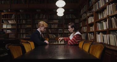 Thoughtful man and woman facing off in a chess game, seated in a peaceful library environment. photo