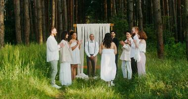 The bride goes to the altar passing by the guests. The groom is waiting her standing near the priest. Wedding in the forest photo