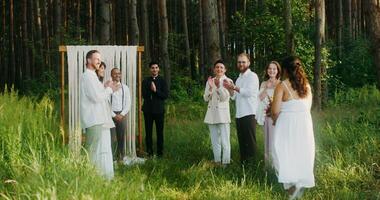The bride walks to the altar passing by the applauding guests. The groom is waiting for her standing near the priest. They kiss when they meet. Wedding in the forest - waiting photo