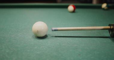cue is aiming at the white ball lying on the billiard table, close-up, the camera repeats the movements of the cue photo