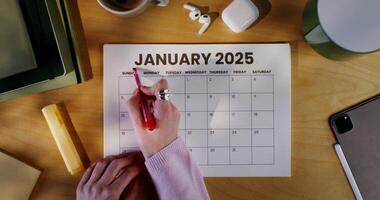 A woman uses a red marker to highlight the month name in her calendar. Zoomed-in view of her hand, person not clearly seen. photo