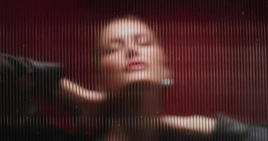 A woman looks at the camera standing behind a striped glass. She's posing in the studio. Close-up of her face photo