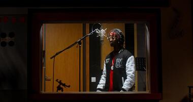 The rapper is recording a song in a recording studio. View through the window from the operator's side photo