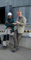 Two workers are eating while sitting on a ramp near the factory. Lunch break at the factory. They're talking. photo