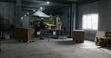 Two men work in a cardboard factory. They take the cardboard cut by the machine and stack it in piles photo