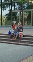 Two women are using a laptop while sitting on the building steps. photo
