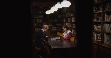 Young man and woman of European appearance playing a chess game, thinking intently, sitting opposite each other at a table in the library photo