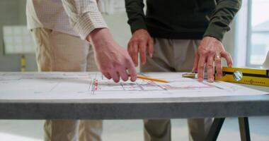 Two men are discussing a house construction project. They are talking standing next to a table in an unadorned room photo