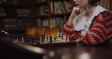 Man and woman of European descent sit across from each other, focused on a chess game in a quiet library. photo