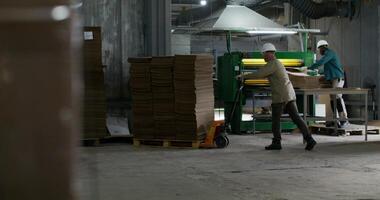Working in a paper mill. One of the men controls the operation of the machine, the second man loads a stack of cardboard onto a cart photo