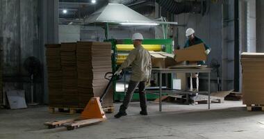 Working in a paper mill. One of the men controls the operation of the machine, the second man loads a stack of cardboard photo