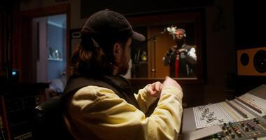 The rapper is recording song in the studio. The sound engineer controls the recording process sitting in the control room photo