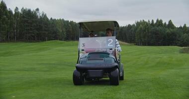 men drive a small electric car across a golf course, chatting with each other. Golf car with passengers, front view photo