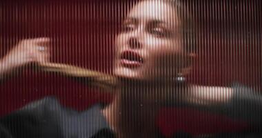 A woman looks at the camera standing behind a striped glass. She's posing in the studio. Close-up photo