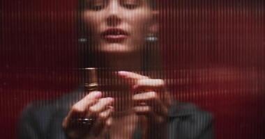 A woman paints her lips with lipstick standing behind a striped glass. She looks at the camera with a serious look. photo