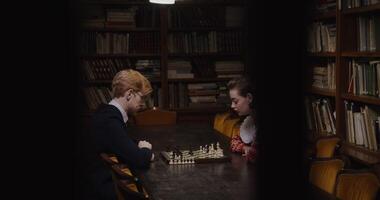Young Caucasian couple playing chess at a table in a library, both deep in thought. photo