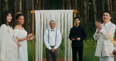 The bride walks to the altar passing by the applauding guests. The groom is waiting for her standing near the priest. They kiss when they meet. Wedding in the forest photo