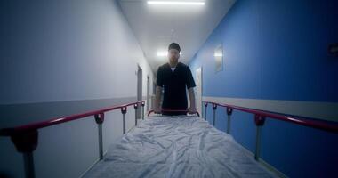 An orderly carries an empty gurney down at the hospital corridor walking backwards photo